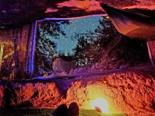 A cozy cave interior with a view of a starry sky through a window, illuminated by soft, warm lighting.