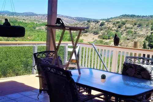 A scenic outdoor patio with a table and chairs, overlooking a green landscape and a bird perched nearby.