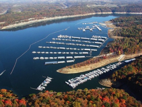 Aerial view of a marina with numerous boats on a calm lake, surrounded by autumn-colored trees and hills.