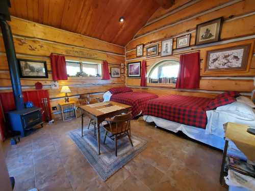 Cozy log cabin interior with two beds, a wooden table, and rustic decor, featuring warm lighting and a fireplace.