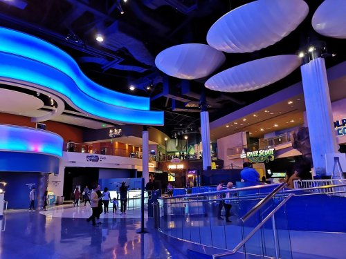 A vibrant indoor space with blue lighting, featuring a modern design and people walking around various entertainment areas.