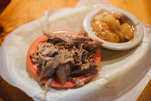 A plate of pulled pork beside a bowl of apple sauce, served on a wooden table.