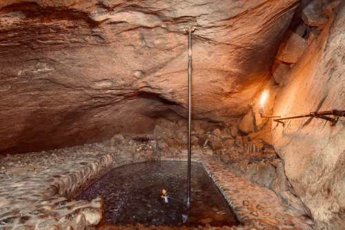 A dimly lit cave with a small pool of water, surrounded by rocky walls and a torch illuminating the scene.
