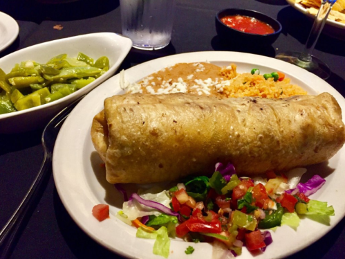 A plate featuring a large burrito, rice, refried beans, salad, and green peppers, with salsa on the side.