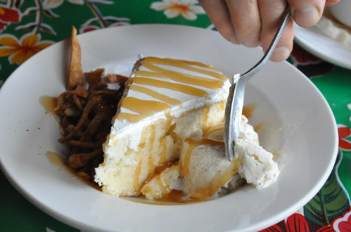 A slice of cake topped with whipped cream and caramel sauce, served with a side of apple pie filling on a colorful table.