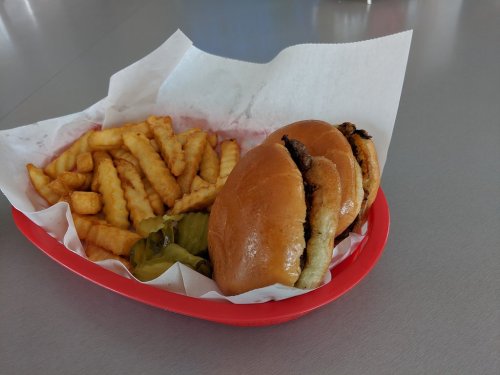 A red tray with two burgers, pickles, and a side of crinkle-cut fries on a gray table.