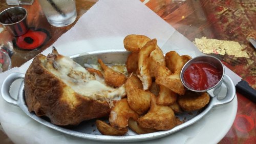 A metal platter with a cheesy sandwich and crispy potato wedges served with a small cup of ketchup.