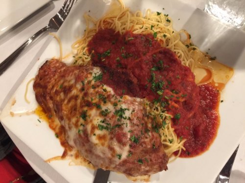 A plate of spaghetti topped with marinara sauce and a cheesy chicken parmesan, garnished with parsley.