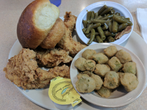 A plate of fried chicken, a bun, green beans, and fried okra with a packet of honey mustard dressing.