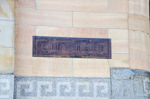 Sign reading "CITY HALL" mounted on a textured stone wall.