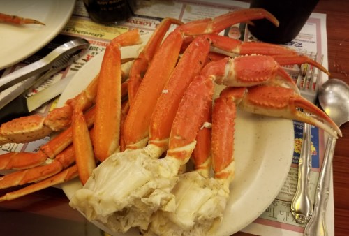 A plate of cooked crab legs, featuring bright orange shells and white meat, served with utensils on a table.