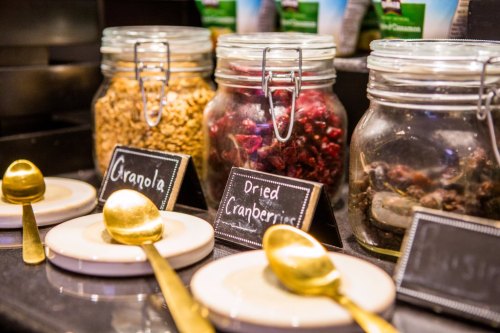 Jars of granola and dried cranberries with gold spoons and labels on a display counter.