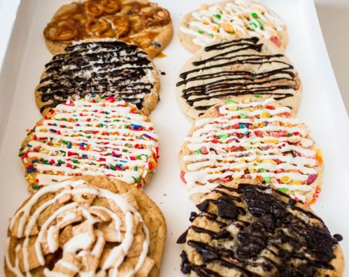 A variety of decorated cookies with colorful toppings and drizzles, arranged neatly on a tray.