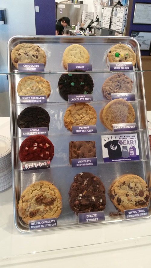 A display of various cookies, including chocolate chunk, sugar, red velvet, and s'mores, arranged on a tray.