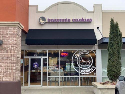 Exterior of Insomnia Cookies shop with a black awning, open sign, and large window displaying cookie offerings.