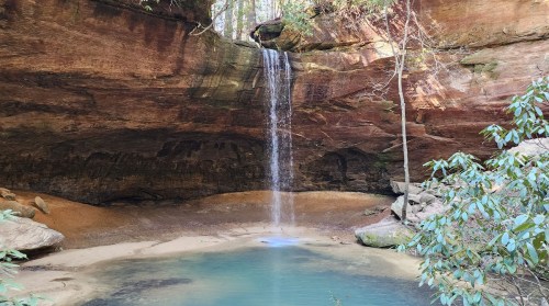 A serene waterfall cascades into a tranquil pool surrounded by rocky cliffs and lush greenery.