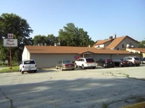 A small building with a sign reading "Pink Poodle," surrounded by parked cars and trees in the background.