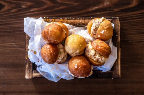 A wooden tray filled with golden, fried dough balls, some split open to reveal a creamy filling, on crumpled white paper.