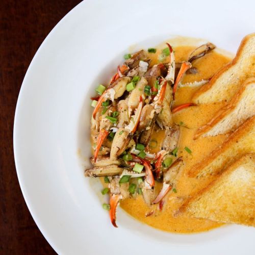 A bowl of crab claws in a creamy sauce, garnished with green onions, served with slices of toasted bread.