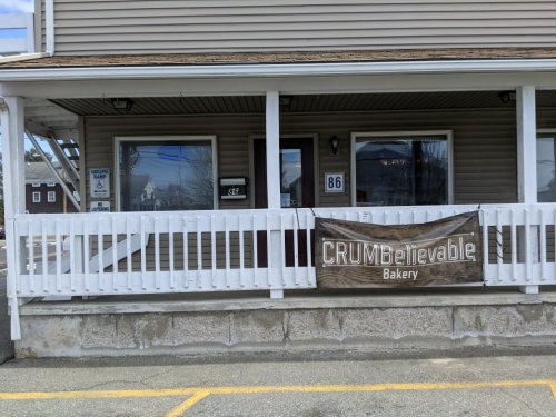 Exterior of CRUMBelievable Bakery with a sign, located at 86, featuring a white railing and a welcoming entrance.