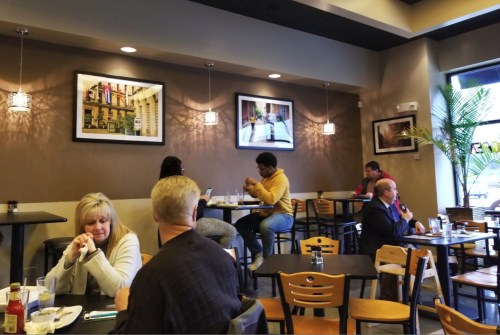 A cozy restaurant interior with patrons at tables, framed photos on the walls, and a plant in the corner.
