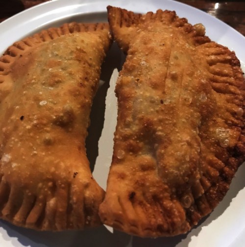 Two golden-brown, crispy empanadas on a white plate, showcasing a flaky crust and a savory filling.