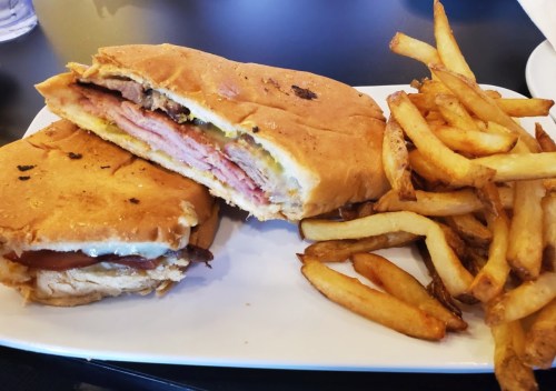 A sandwich with layers of meat and cheese, served with a side of golden French fries on a white plate.