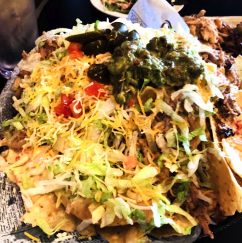 A large plate of nachos topped with shredded lettuce, cheese, jalapeños, salsa, and guacamole.