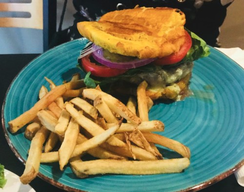 A colorful burger with lettuce, tomato, and onion, served with a side of golden French fries on a blue plate.
