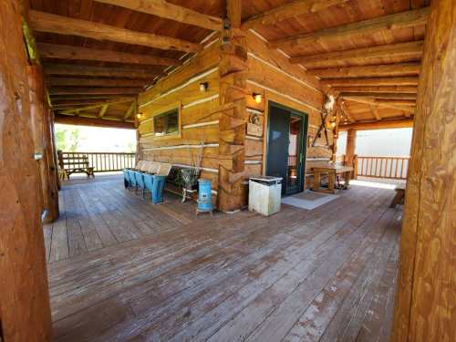 A rustic wooden porch with seating, a table, and a view of nature, featuring log cabin architecture.