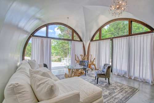 Bright, modern living room with arched windows, white sofa, glass table, and elegant decor. Natural light floods the space.