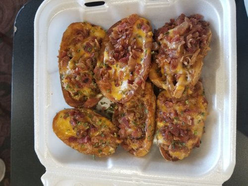A takeout container filled with cheesy, bacon-topped potato skins garnished with herbs.