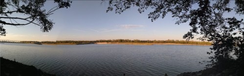A panoramic view of a calm river surrounded by trees under a clear blue sky.