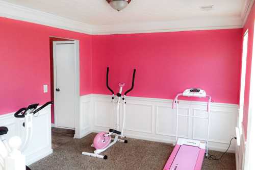 A bright pink room with exercise equipment, including a treadmill, elliptical, and a pink exercise ball.