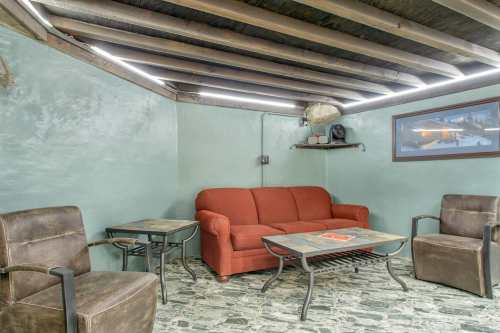 Cozy basement lounge with a red sofa, two brown chairs, and a stone table under a wooden ceiling with LED lighting.
