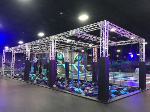 A colorful indoor obstacle course with climbing structures and foam pits, illuminated by vibrant lights.