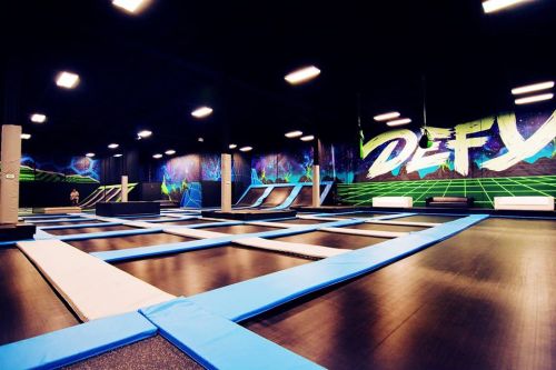 A spacious indoor trampoline park with blue trampolines and vibrant graffiti on the walls.