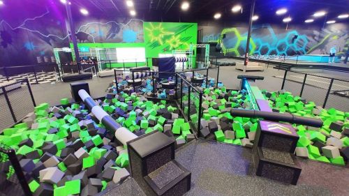 A vibrant indoor trampoline park featuring foam pits, climbing structures, and colorful walls.