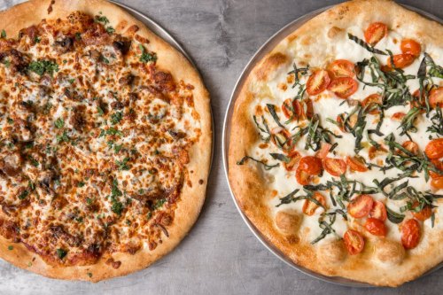 Two pizzas on metal trays: one topped with sausage and cheese, the other with tomatoes and basil on a white sauce.