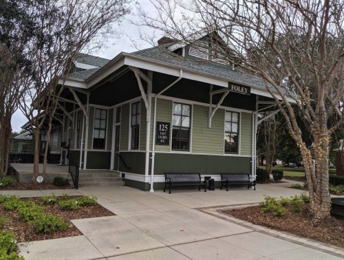 Historic green train station with "FOLEY" sign, surrounded by trees and landscaped pathways.