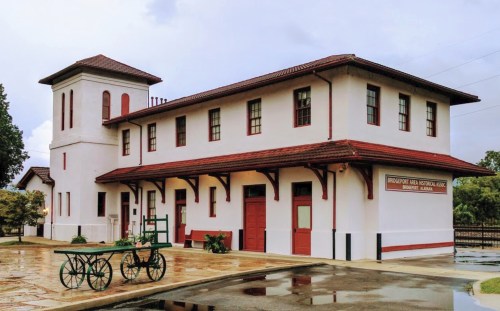 Historic building with a red-tiled roof, white walls, and a vintage cart in front, set in a scenic outdoor area.