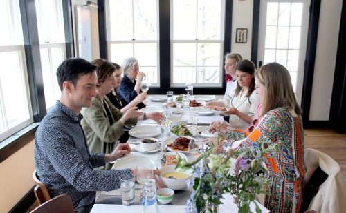 A group of people enjoying a meal together at a dining table, with various dishes and a floral centerpiece.