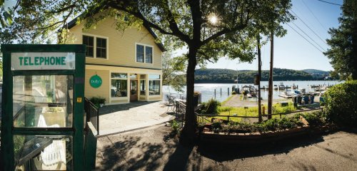 A scenic view of a waterfront restaurant with a telephone booth, boats, and lush greenery along the shore.