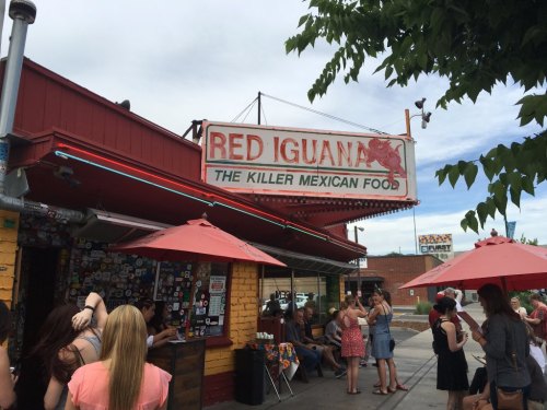A colorful restaurant exterior with a sign reading "Red Iguana: The Killer Mexican Food" and outdoor seating under umbrellas.