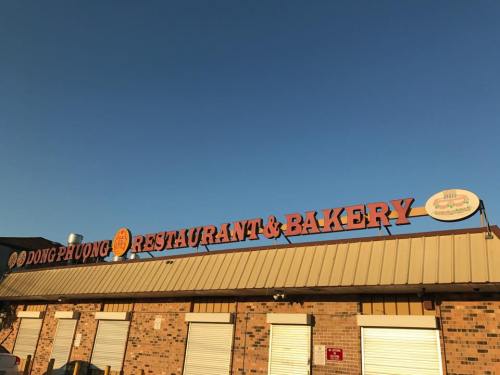 Sign for Dong Phuong Restaurant & Bakery against a clear blue sky, featuring orange lettering on a brick building.