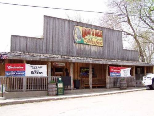 A rustic bar with wooden exterior and signage, featuring banners for Budweiser and a biker theme.
