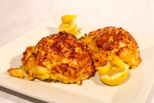Two golden-brown crab cakes served with lemon wedges on a white plate.