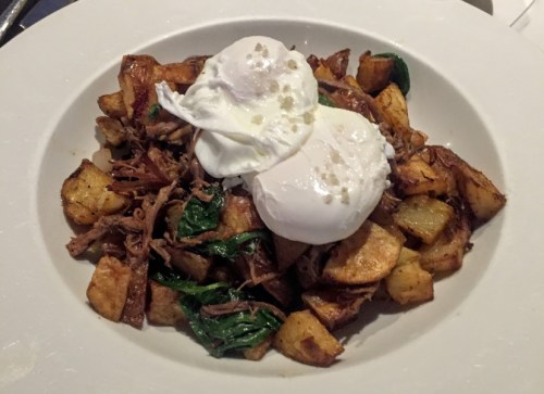 A plate of crispy potatoes topped with pulled meat, spinach, and two poached eggs.