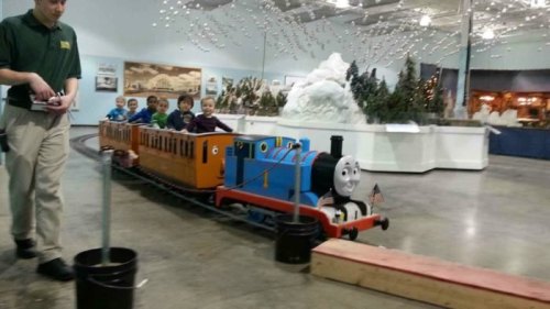 A miniature train with children riding inside, passing by a display of snowy mountains and festive decorations.
