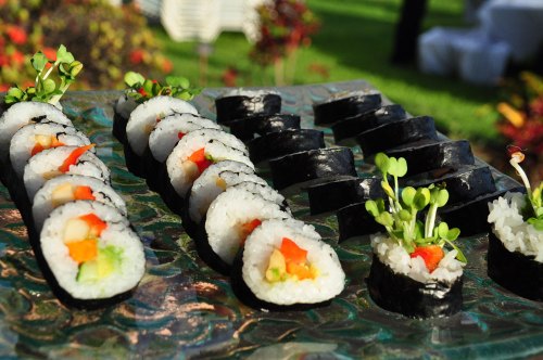 A platter of assorted sushi rolls, featuring colorful vegetables and garnished with fresh sprouts, set outdoors.